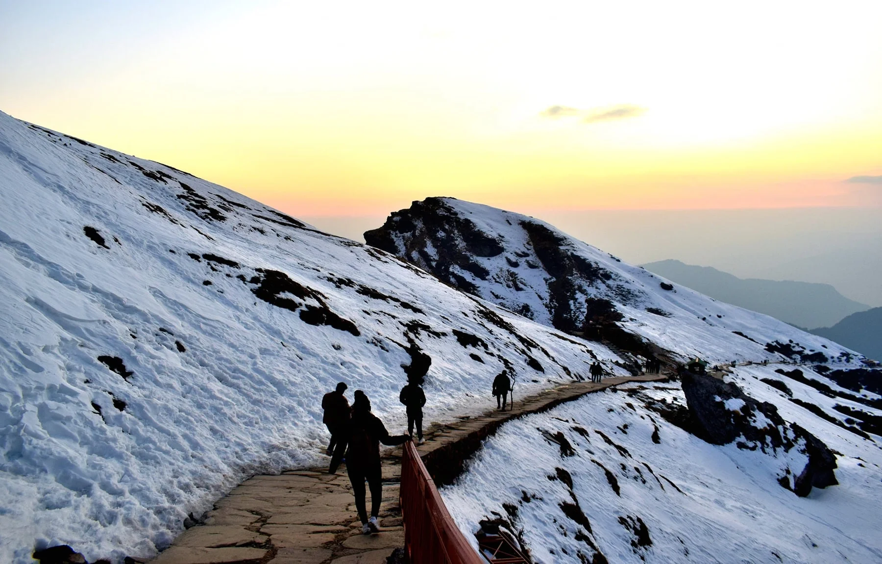 MyHillTour Uttarakhand Tour Package.-Trekkers walking along a snow-covered trail in the Himalayan mountains at sunrise.