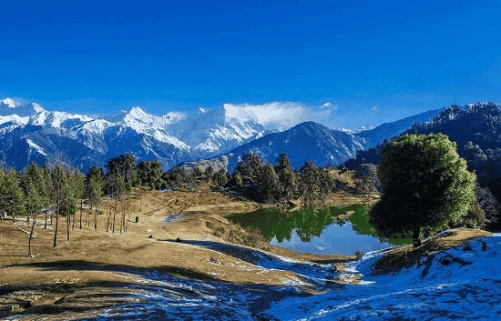 Scenic view of Deoria Tal lake with snow peaks and pine forest in Deoria Tal Trekking Package